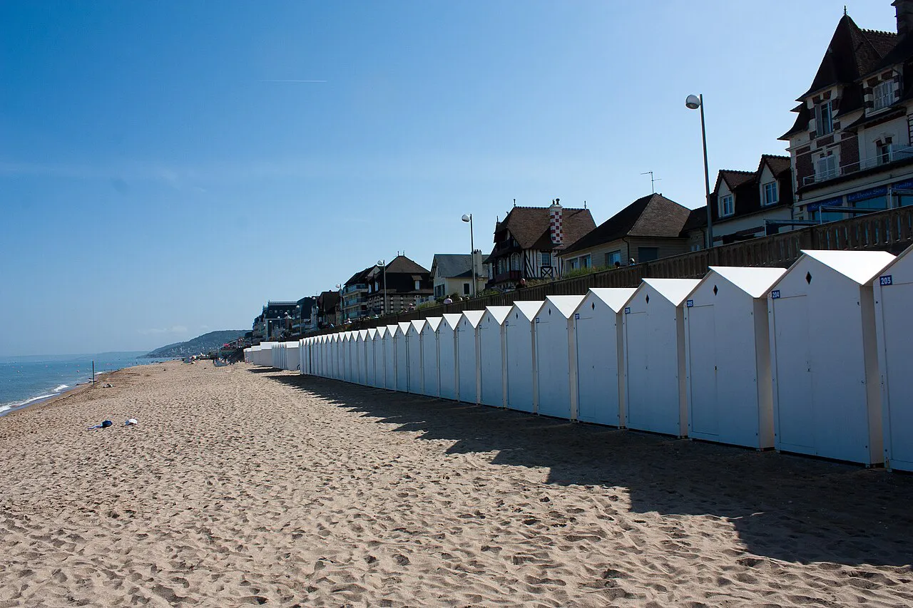 Row of white beach huts along the sand at Cabourg, with seafront villas behind