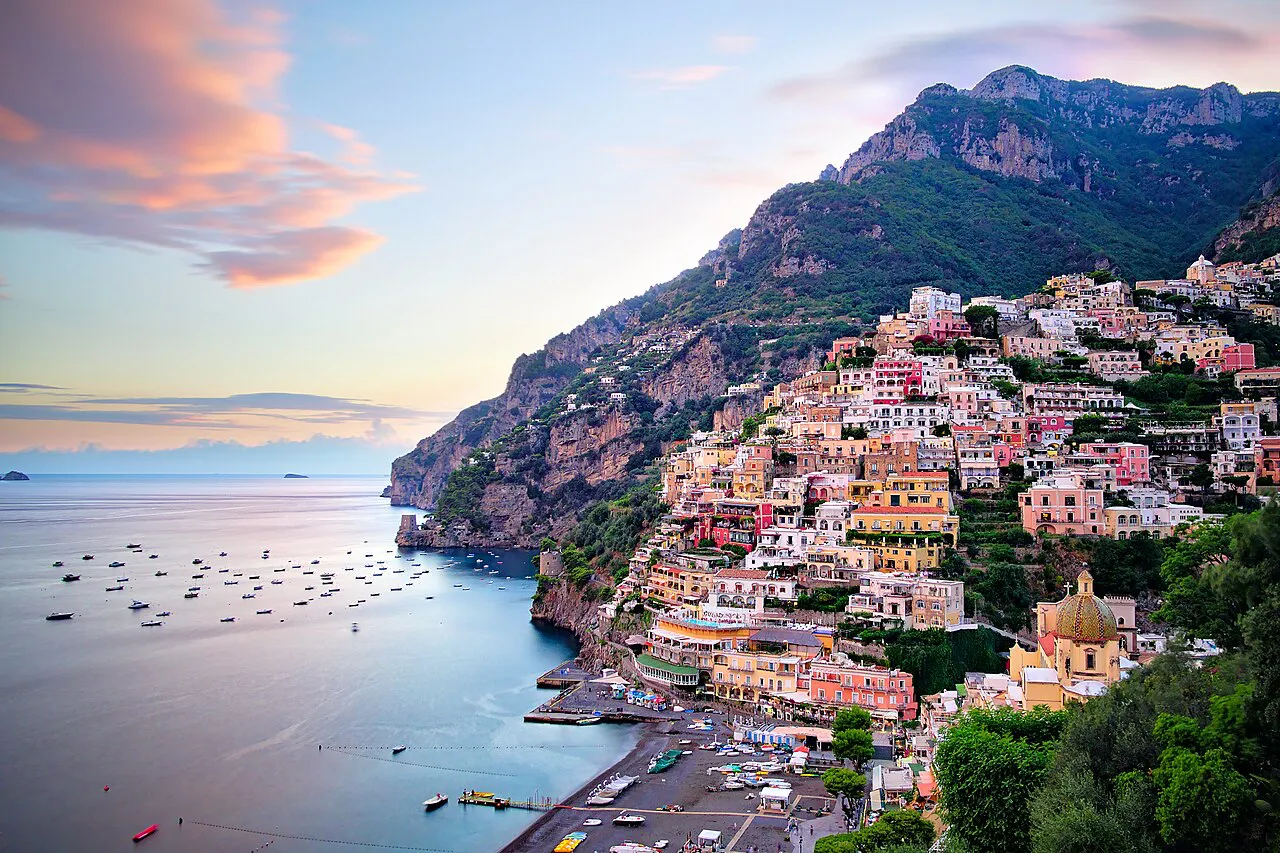 Positano's pastel hillside village and the church dome above the bay under a pink evening sky