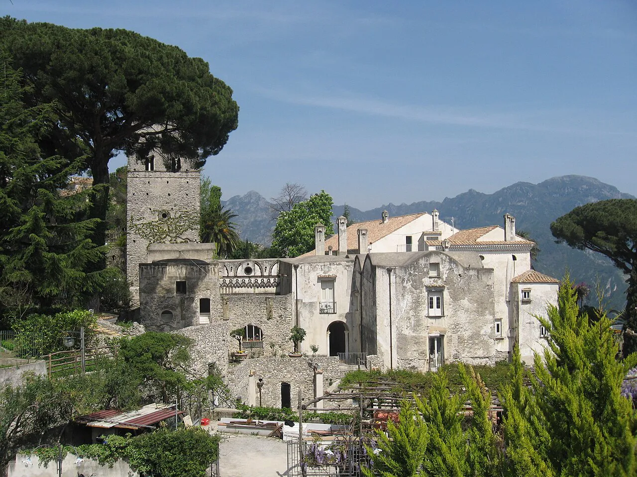 Stone tower and medieval buildings of Villa Rufolo among umbrella pines in Ravello, mountains behind