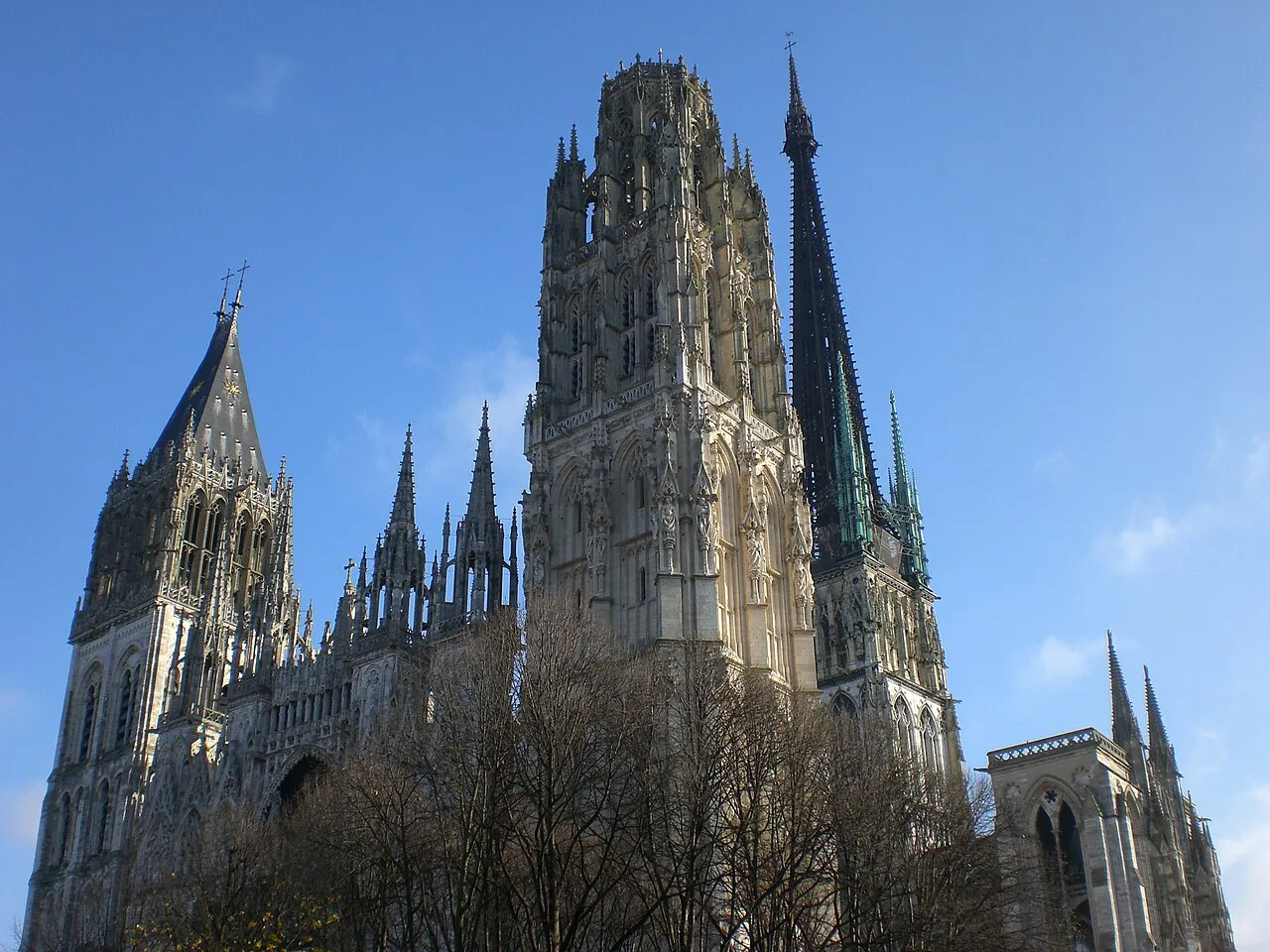Gothic towers and the tall iron spire of Rouen Cathedral rising against a clear blue sky