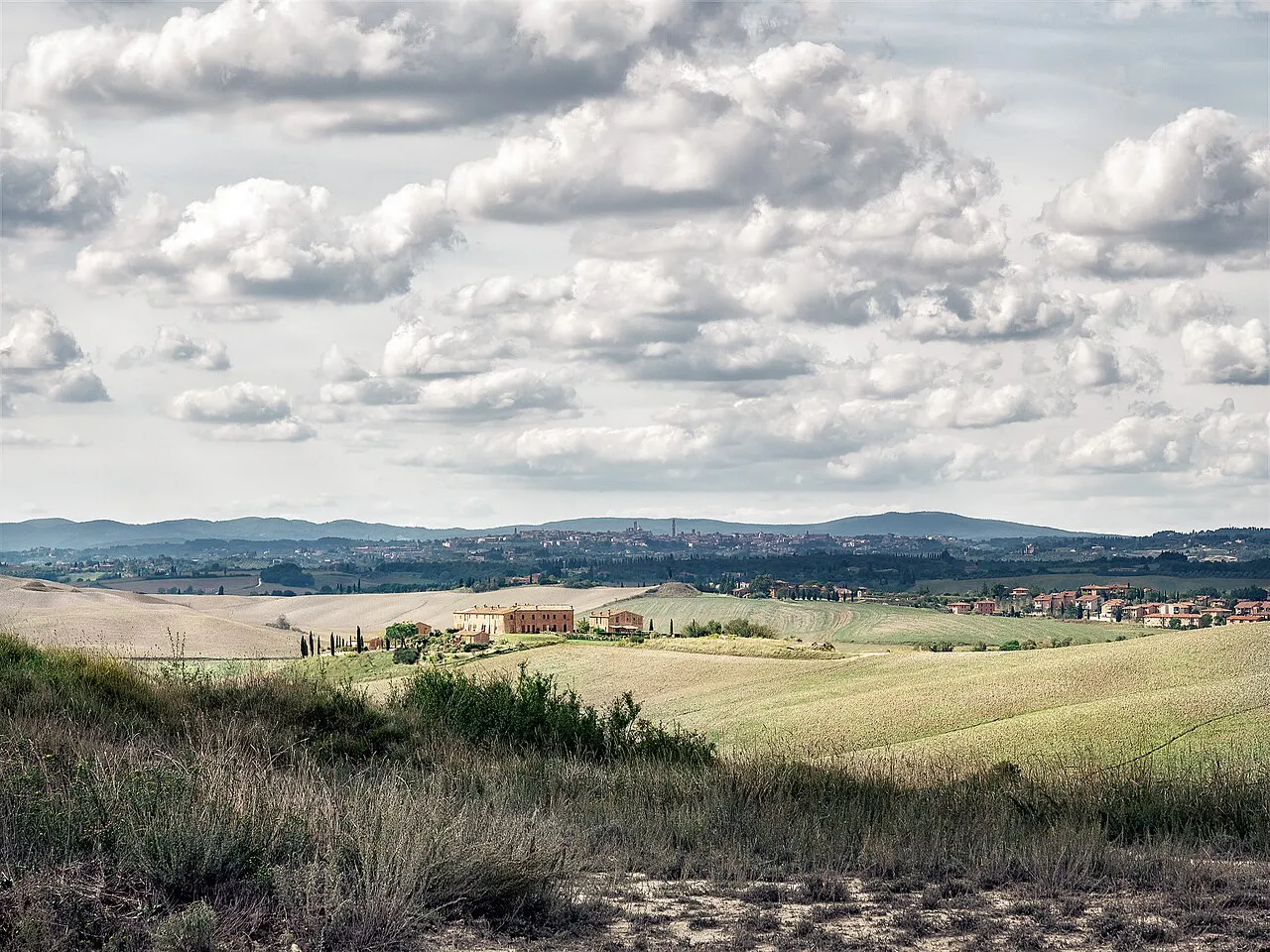 Rolling grassy hills of the countryside outside Siena under a wide sky of scattered clouds, Tuscany