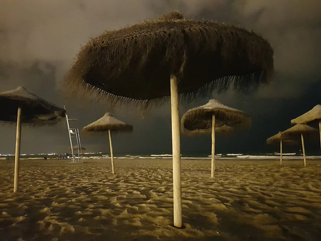 Thatched beach parasols on the sand of Malvarrosa beach in Valencia under a dark evening sky