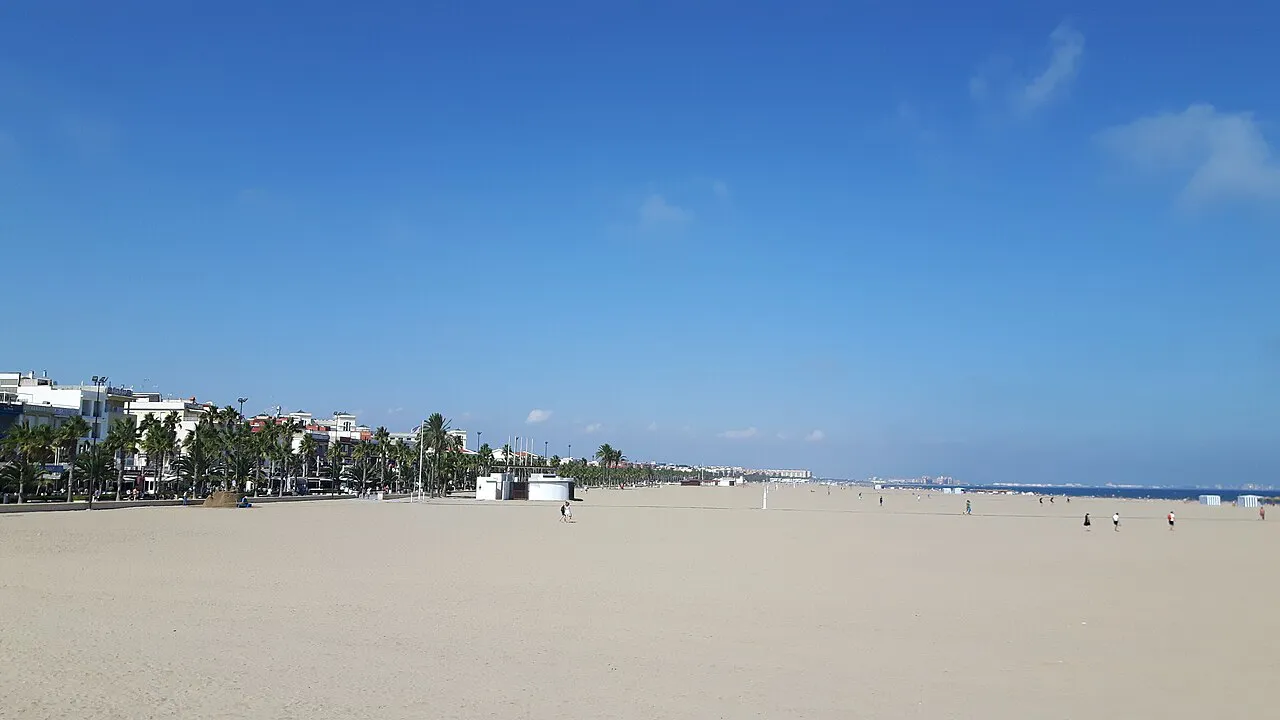 Wide sandy Malvarrosa beach in Valencia with the palm-lined seafront promenade in the distance