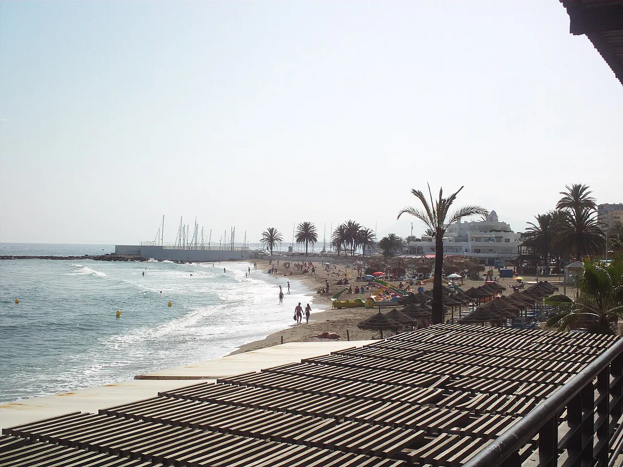 Public beach just south of Marbella's old town, with palms, parasols and the marina breakwater beyond