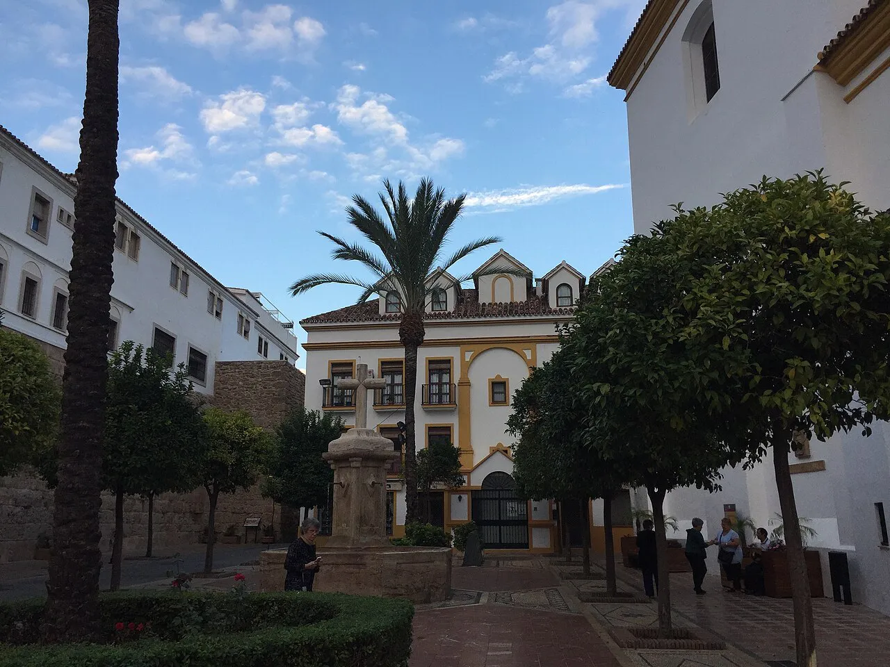 Quiet Old Town square in Marbella with orange trees, a tall palm and a historic church facade