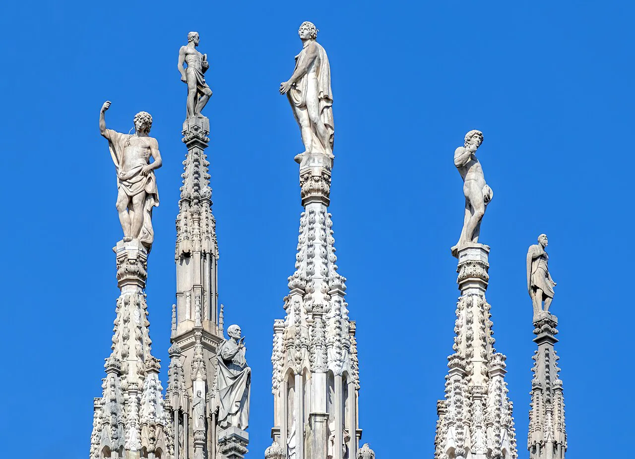 Marble statues crowning the Gothic spires of Milan Cathedral against a deep blue sky