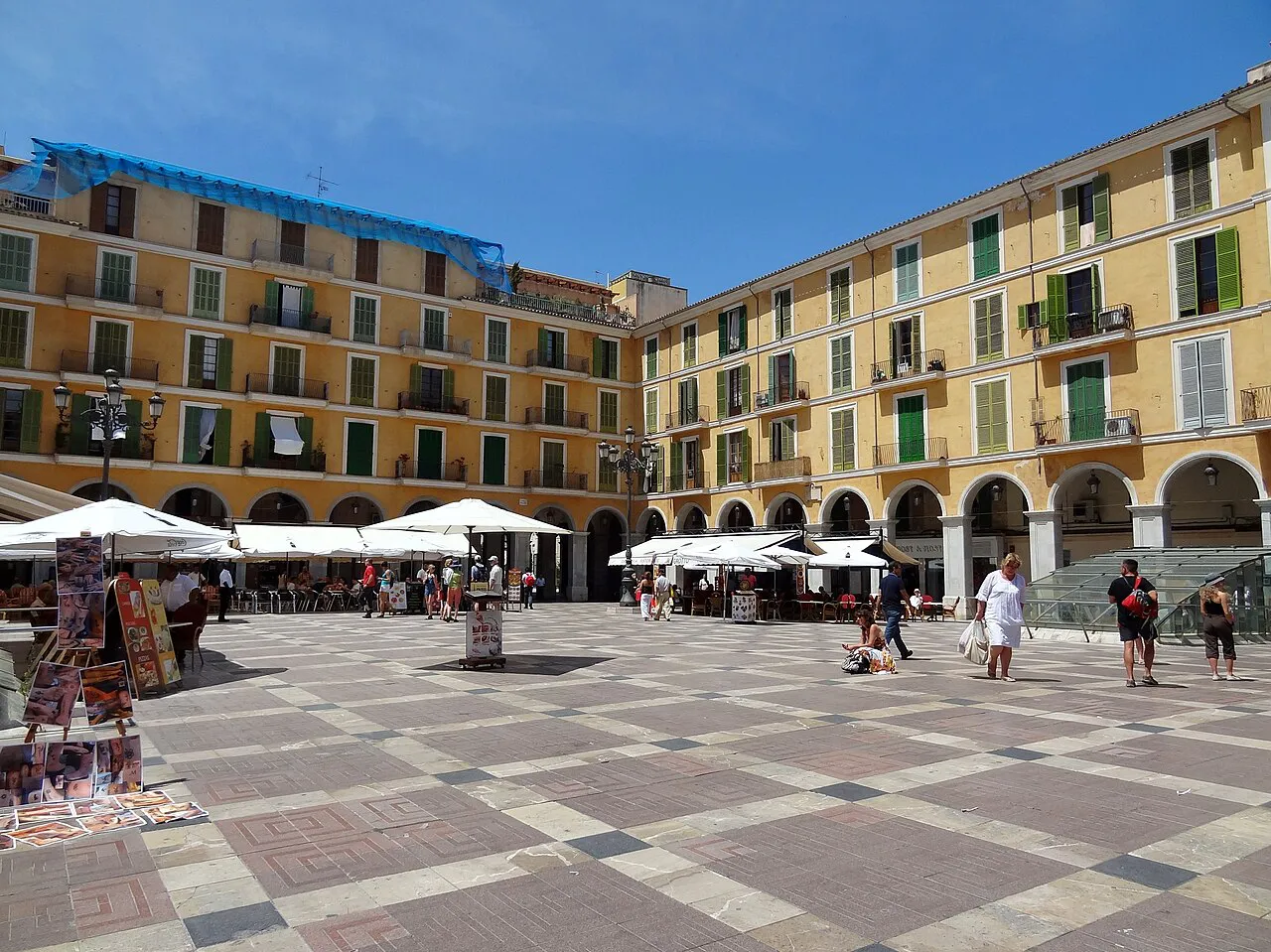Arcaded ochre facades around the paved Plaça Major in central Palma under a blue sky