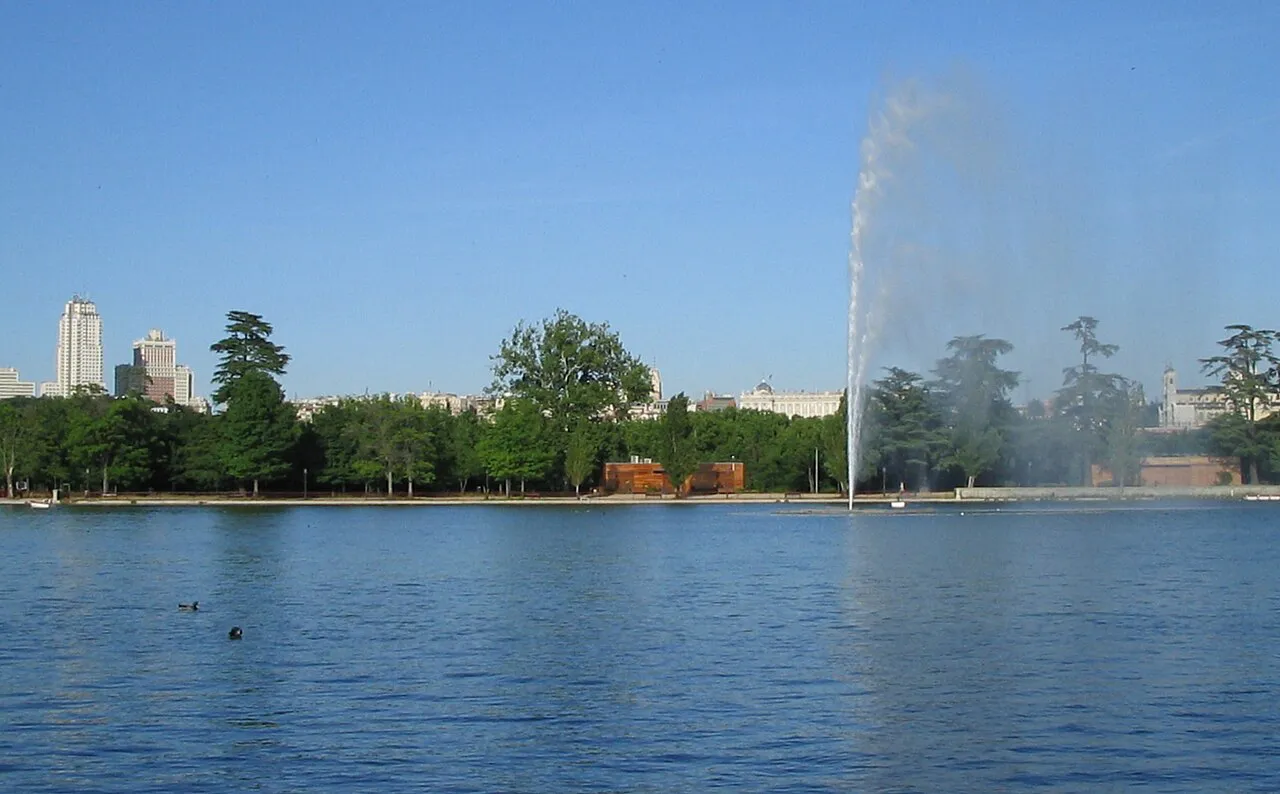 Casa de Campo lake in Madrid with a tall fountain and the city skyline beyond the trees