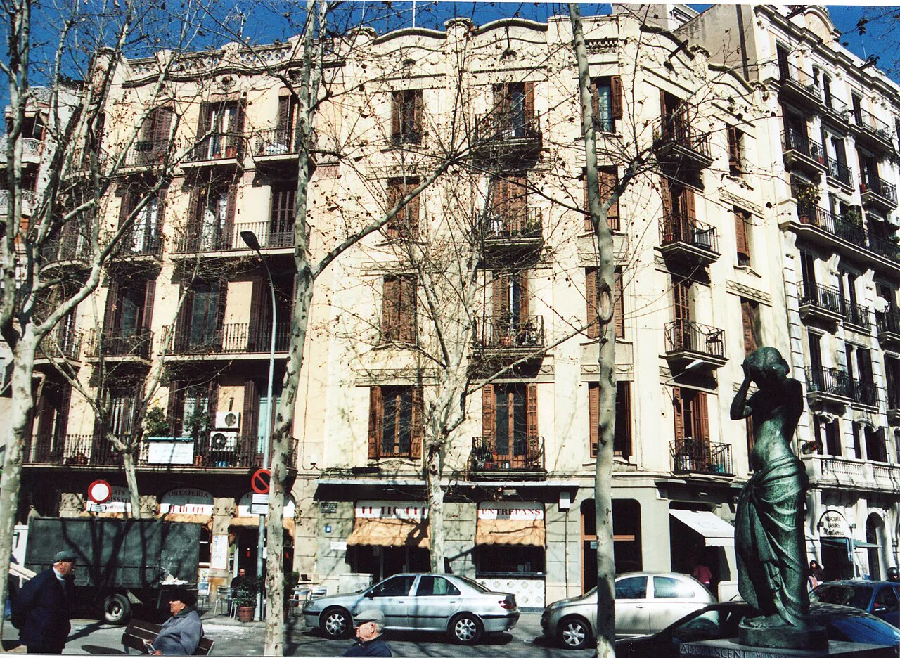 Ornate apartment buildings and a bronze statue among the plane trees of Rambla del Poblenou, Barcelona