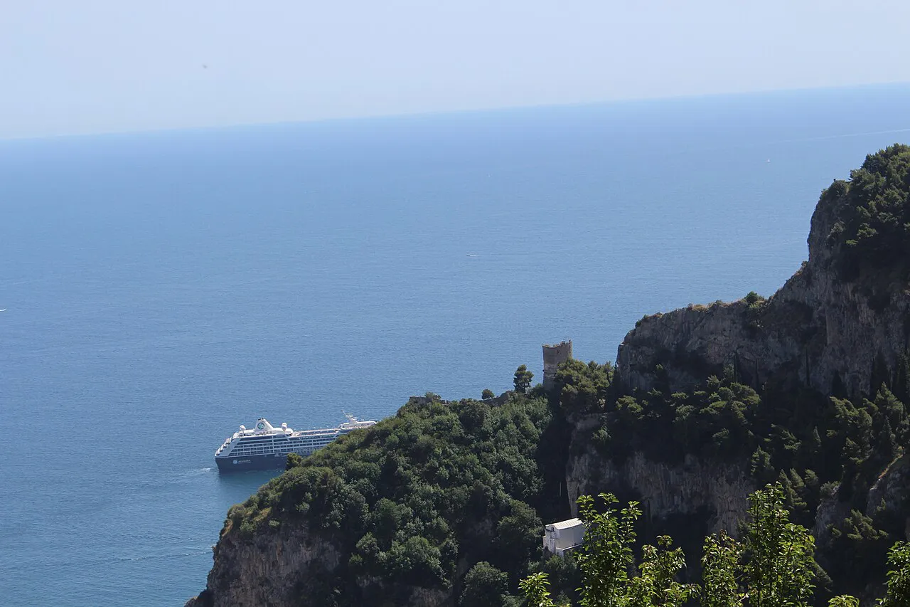 Wooded cliffs dropping to the open sea below Ravello, with a cruise ship offshore on the Gulf of Salerno