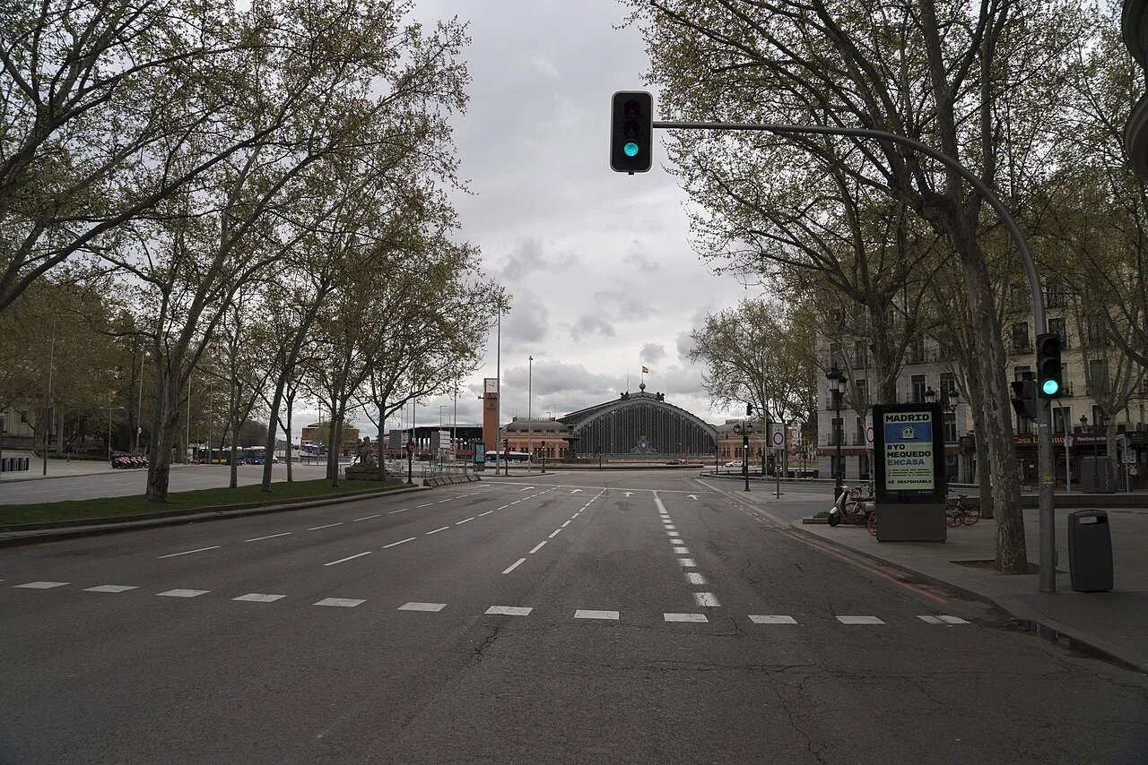 Wide, empty lower Calle de Atocha lined with trees, with Atocha station visible at the far end, Madrid