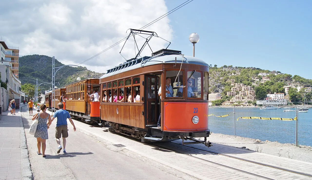 Orange vintage tram running along the seafront at Port de Sóller, with the bay and hills beyond
