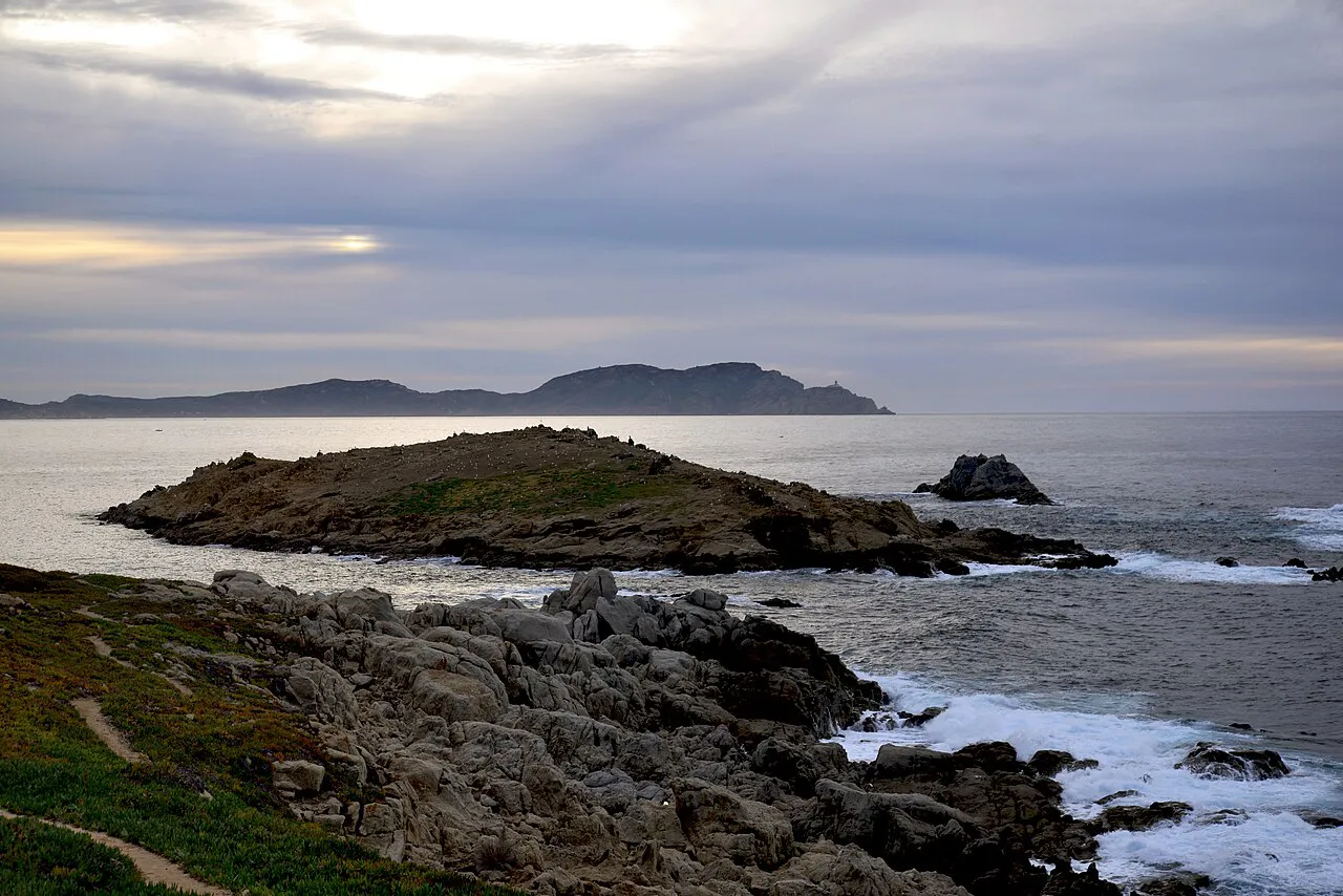 Rocky shoreline and the small Spano islet at Lumio on the Balagne coast under a soft evening sky