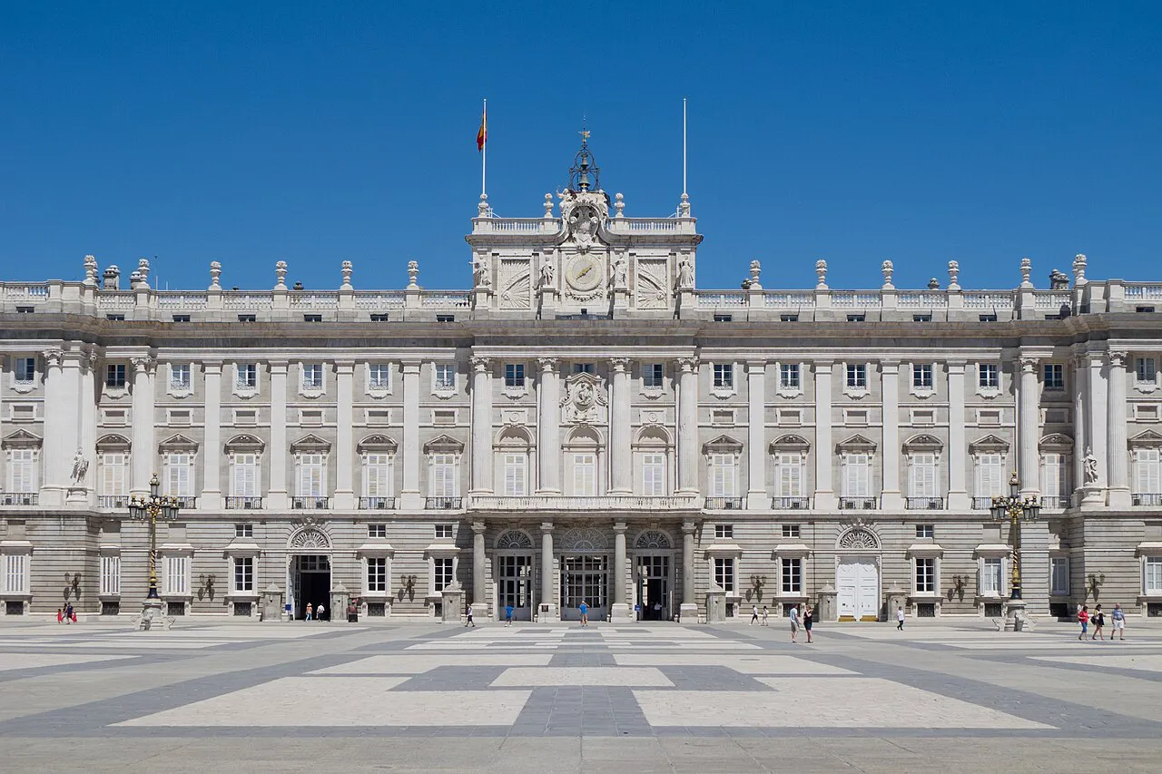 South façade of the Royal Palace of Madrid seen across the paved Plaza de la Armería under a blue sky