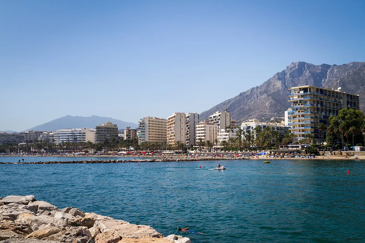 Marbella's seafront and beaches seen across the water from a rocky breakwater, with Sierra Blanca behind