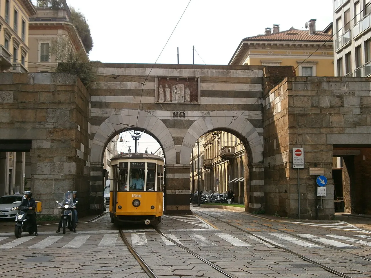 Striped medieval Archi di Porta Nuova gateway in Milan with a yellow tram passing beneath