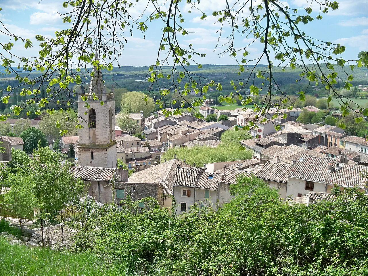 Tiled rooftops and church bell tower of Mane seen through spring branches