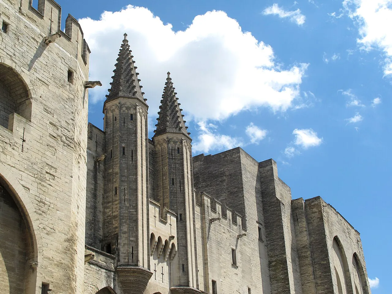 Gothic towers and stone walls of the Palais des Papes against a blue sky in Avignon