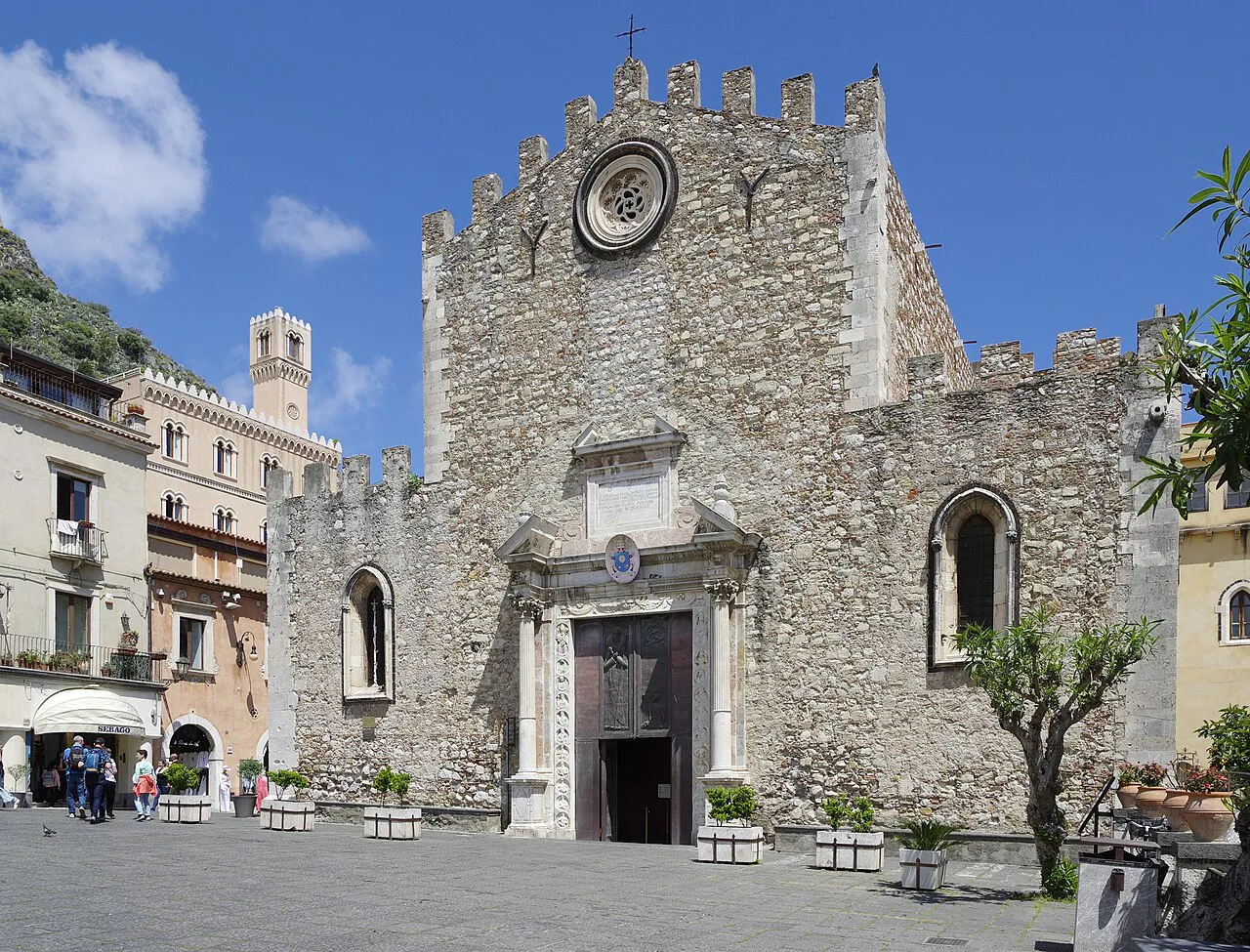Crenellated stone facade of Taormina Cathedral on Piazza Duomo under a blue sky
