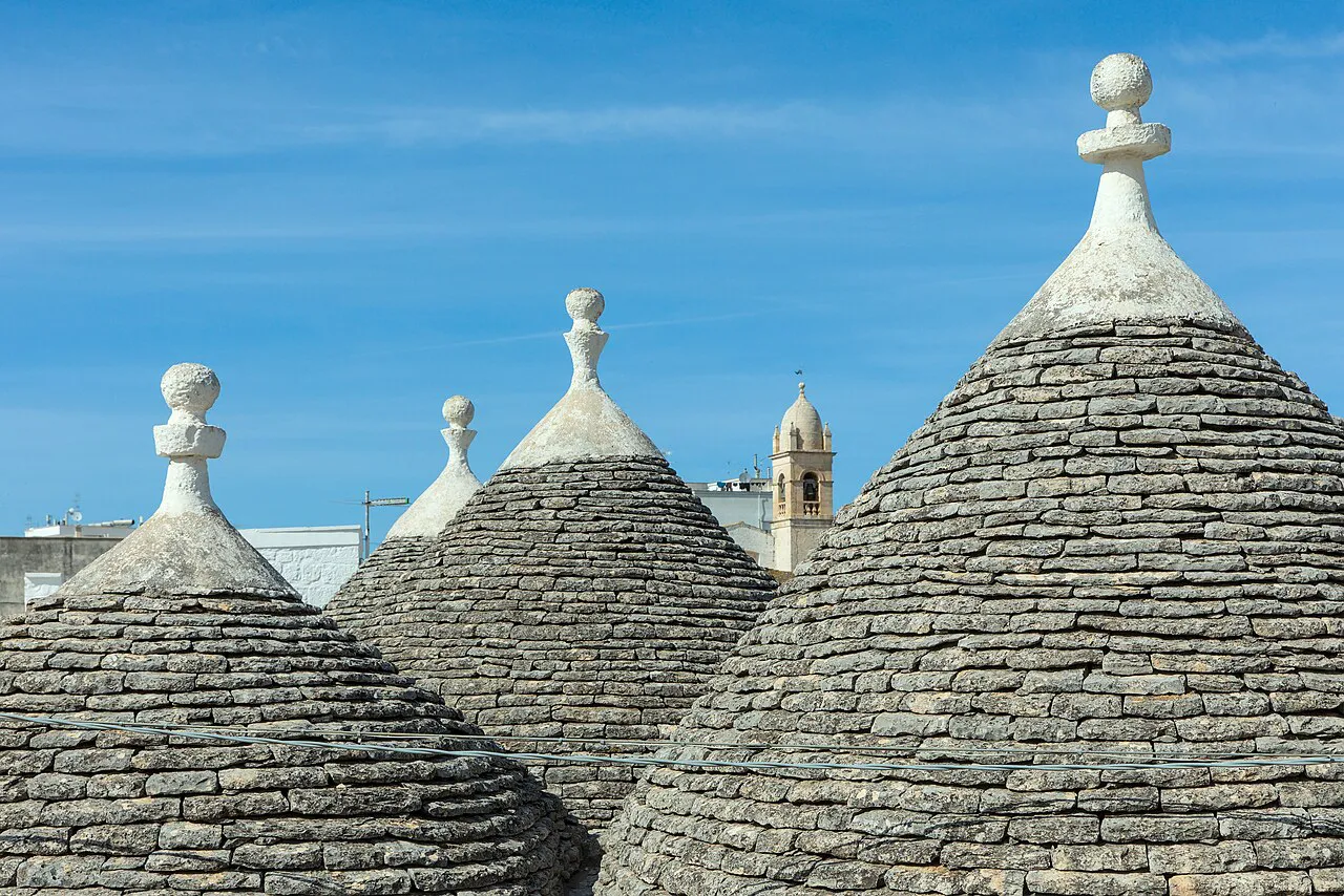 Close view of grey stone trulli cones with white pinnacles against a blue sky in Rione Monti, Alberobello