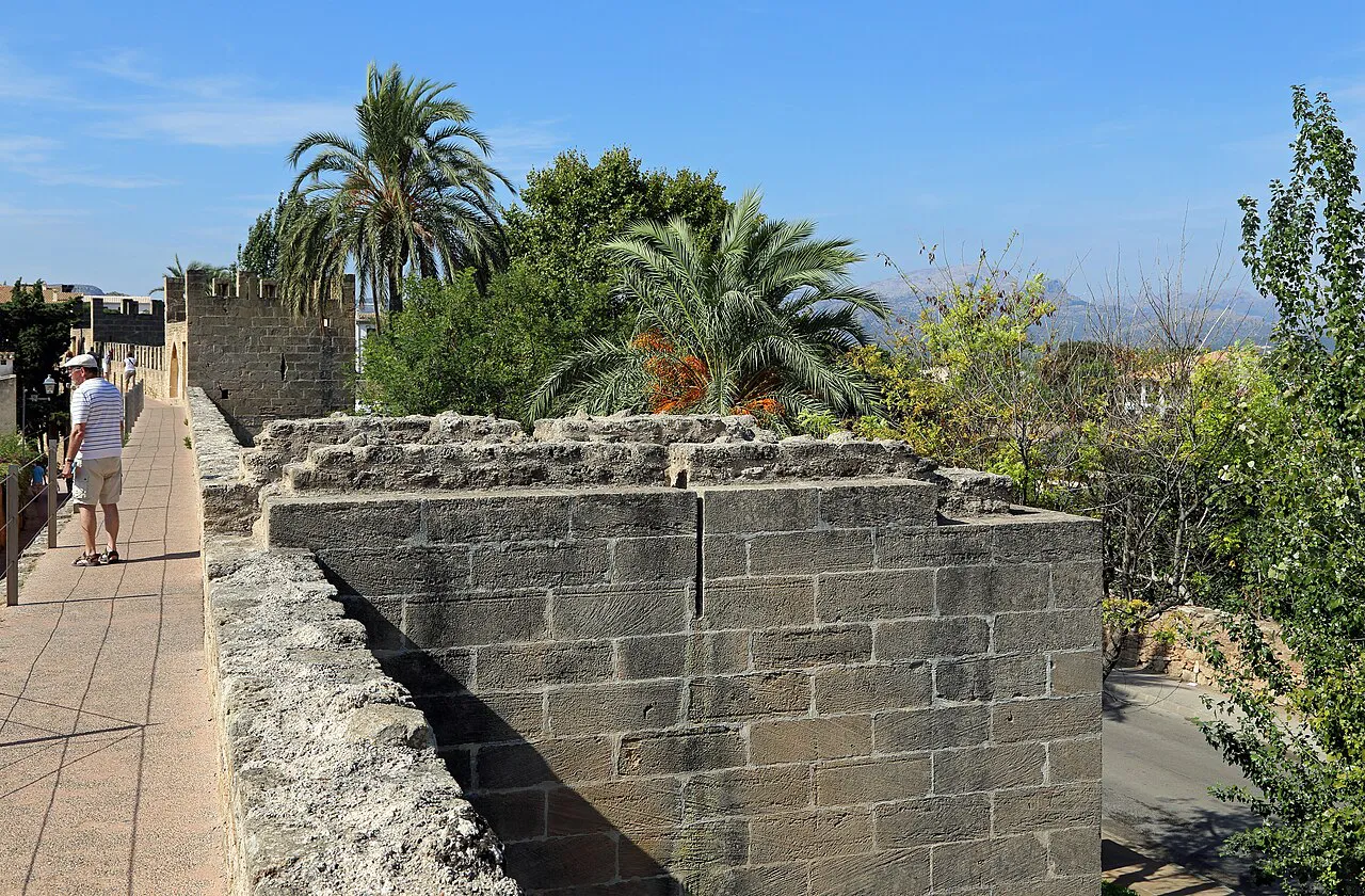Walkway along the top of the medieval city walls of Alcúdia, with battlements and palm trees