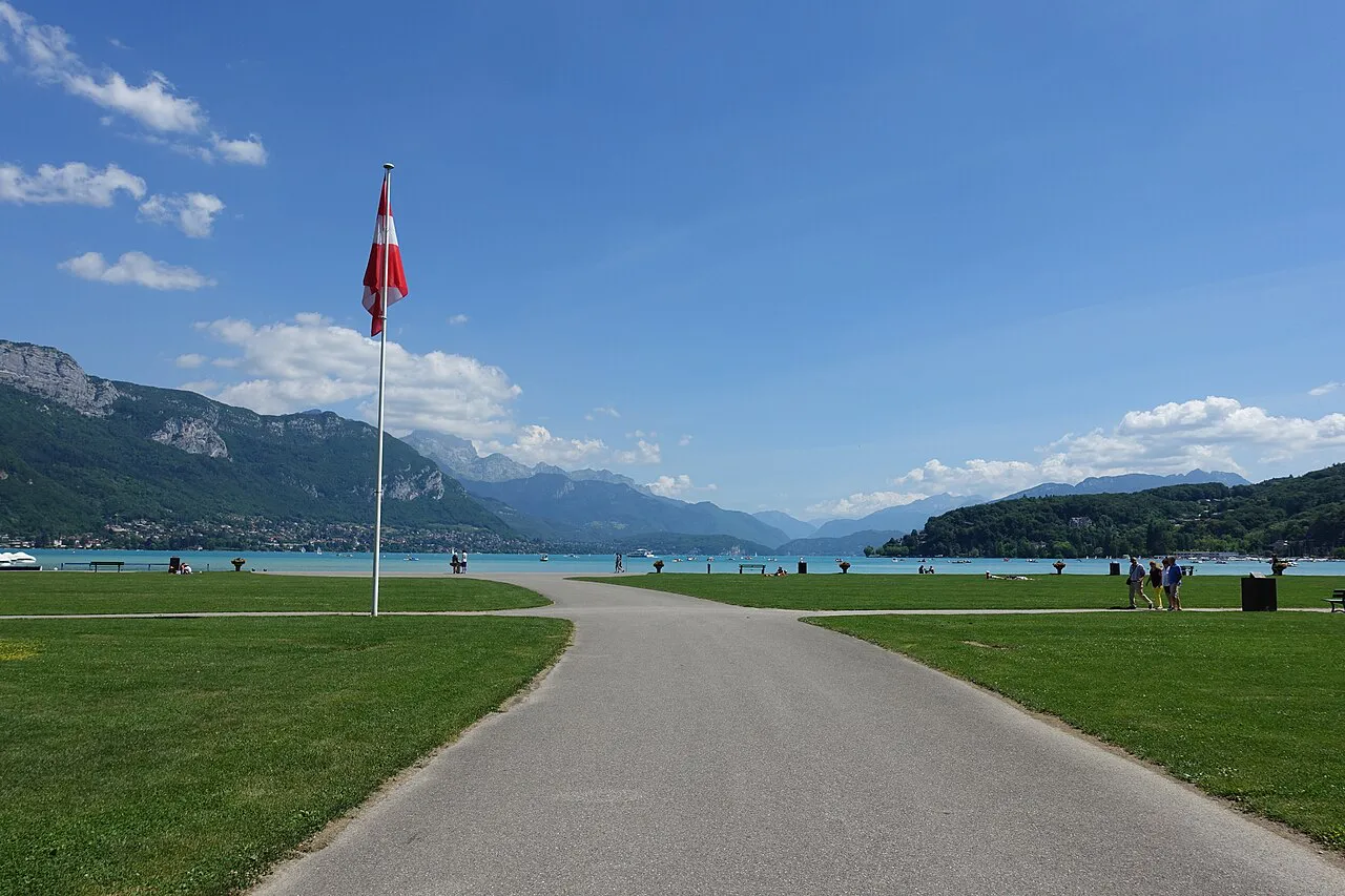 Path across the open lawns of the Pâquier towards Lake Annecy and the mountains