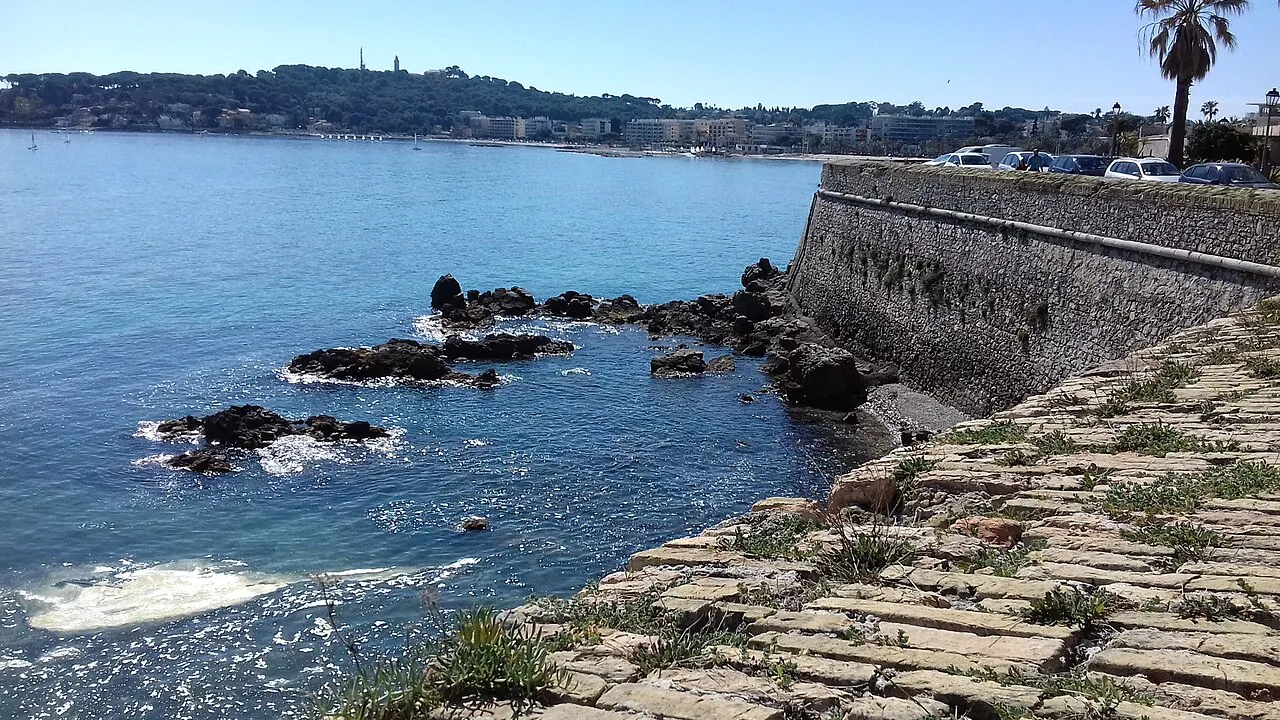 Stone sea wall of the Antibes ramparts above dark rocks and clear Mediterranean water