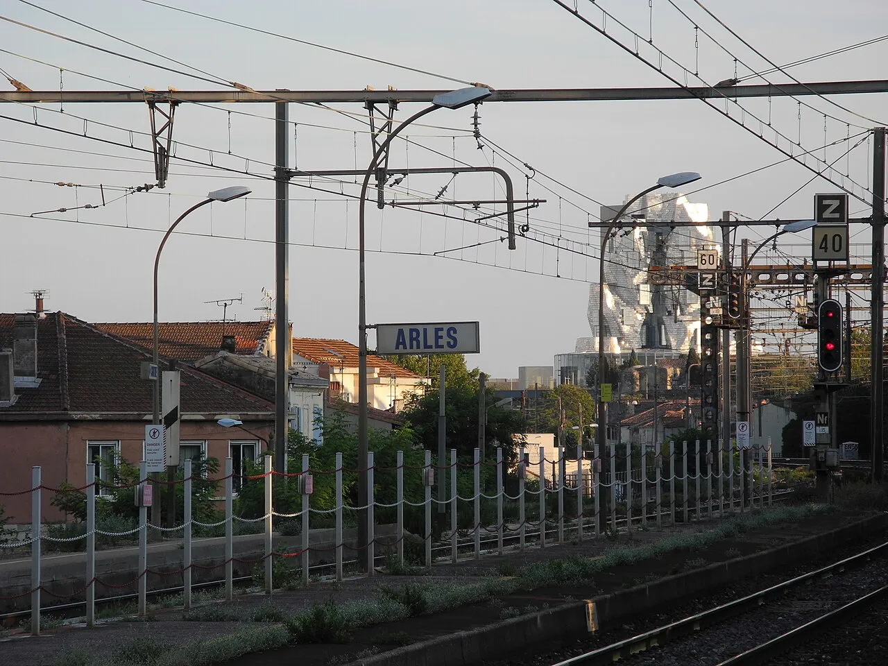 Platform sign at Arles railway station with tracks, overhead lines and the LUMA tower in the distance
