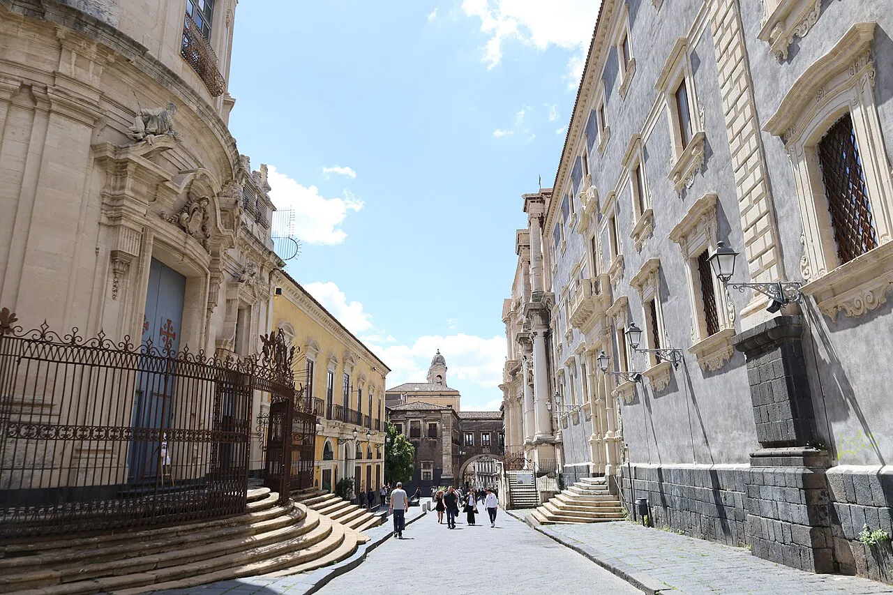 Baroque church railings and palazzi lining Via dei Crociferi in Catania, with an arch at the far end