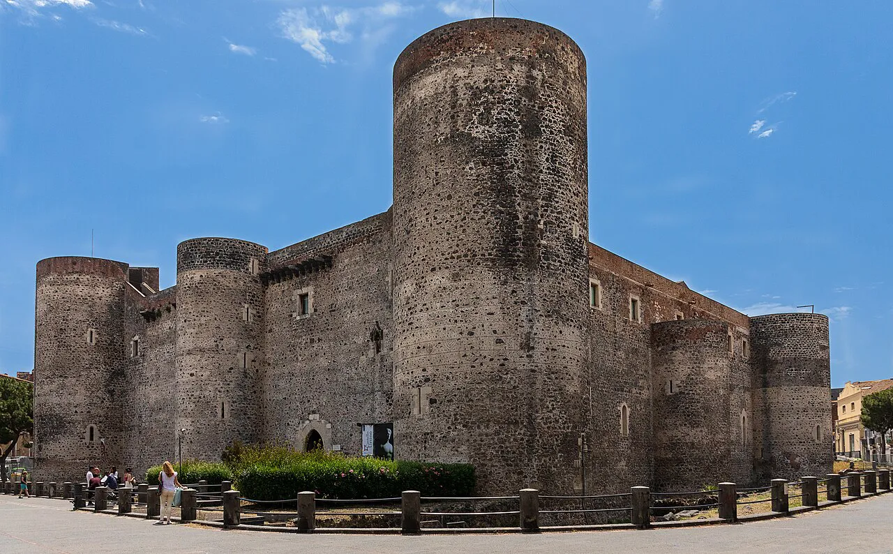 The dark lava-stone towers and walls of Castello Ursino in Catania under a blue sky