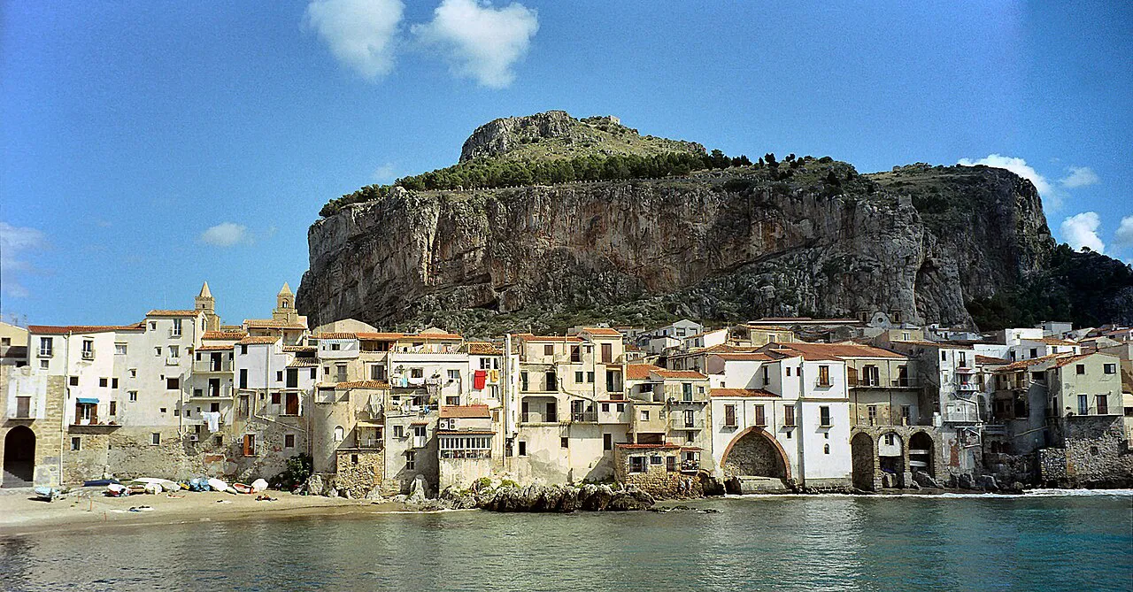 Old waterfront houses of Cefalù lining a small beach beneath the great rock of the Rocca