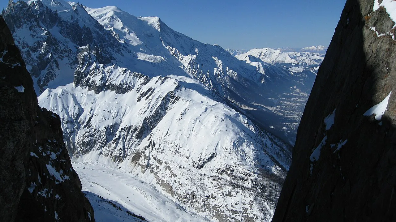 Snowy slopes and the Chamonix valley toward Mont Blanc, framed by dark rock walls at the Grands Montets