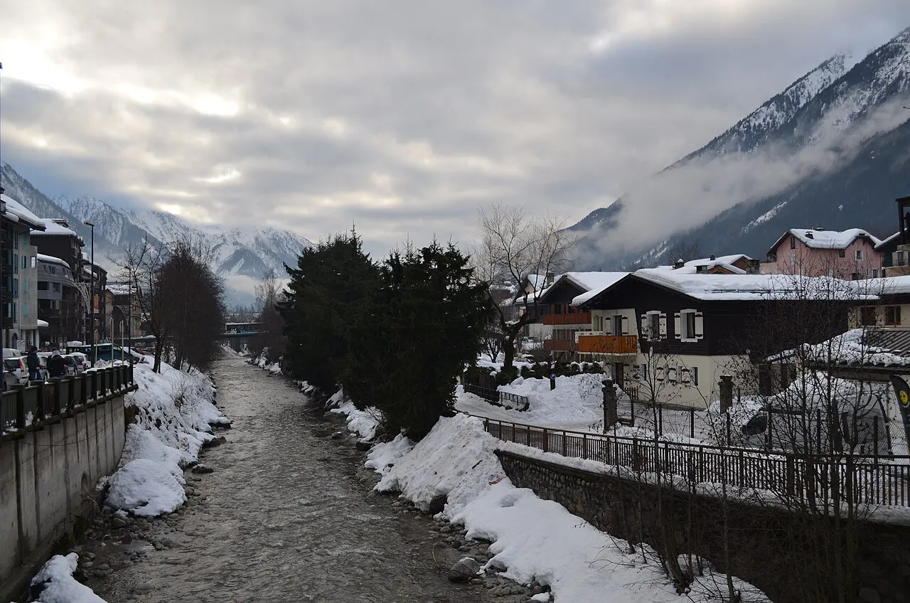The Arve river between snowy banks and chalets in Chamonix town in winter, mountains in cloud