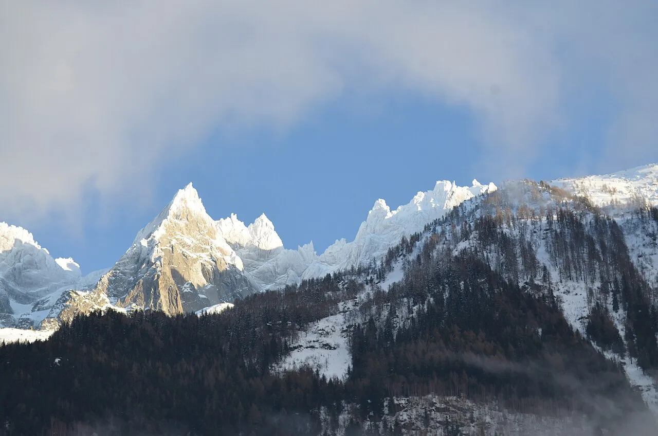 Sunlit snowy granite needles of the Aiguilles de Chamonix above dark forested slopes in winter