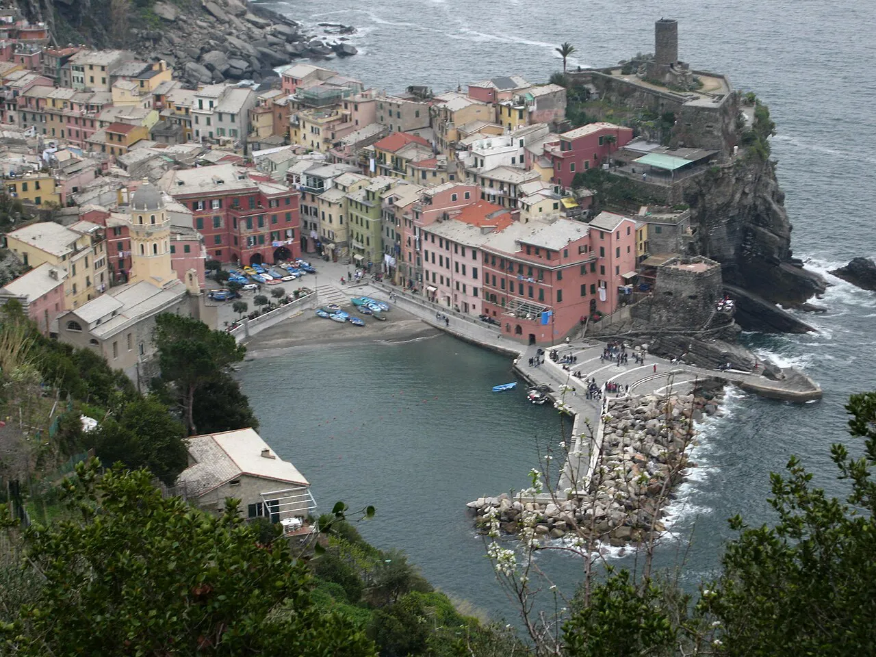Vernazza's pastel houses, small harbour and castle tower on a rocky point, seen from the hillside above
