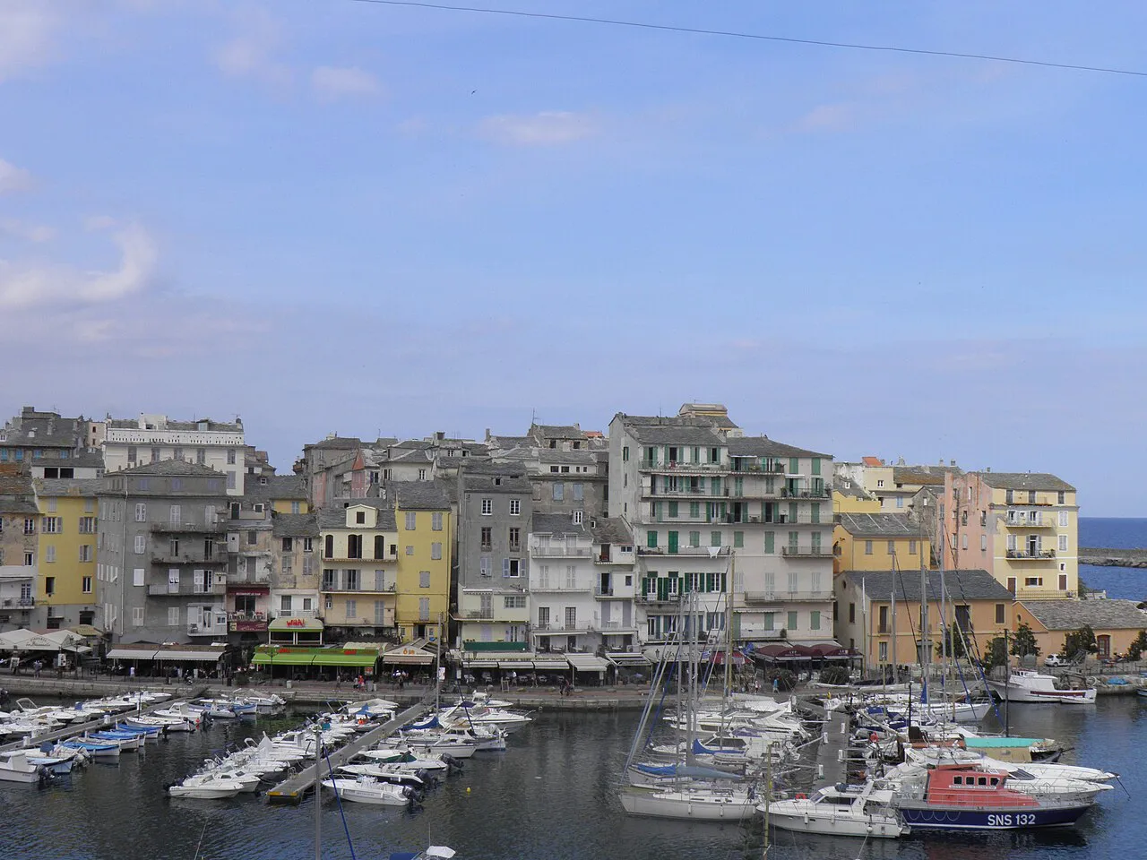 Colourful tall buildings lining the Old Port of Bastia with moored boats in the foreground