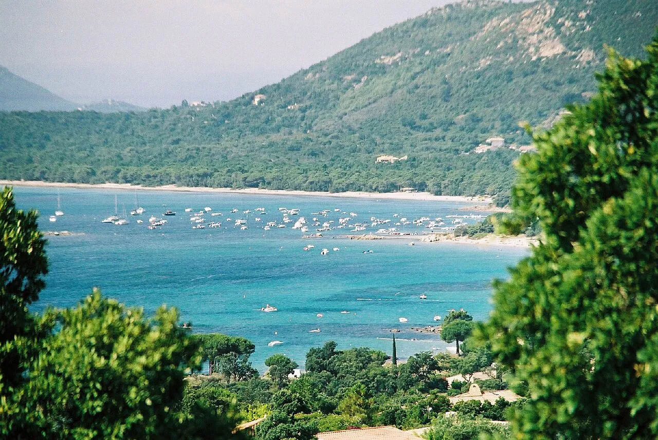 Turquoise Pinarellu bay with boats and a sandy shore below wooded hills near Pinarello