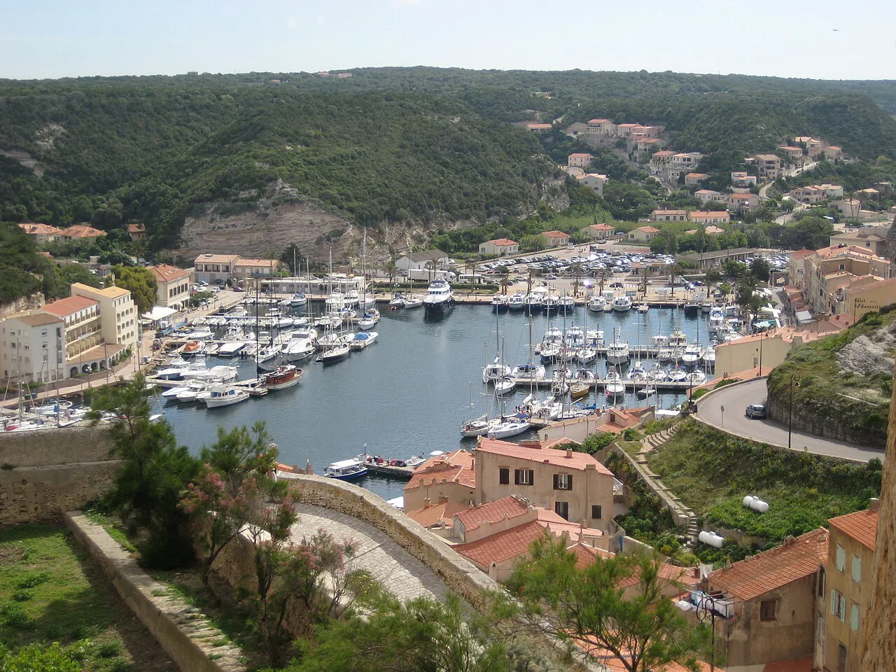 Bonifacio harbour full of moored boats below green hills and the town's houses