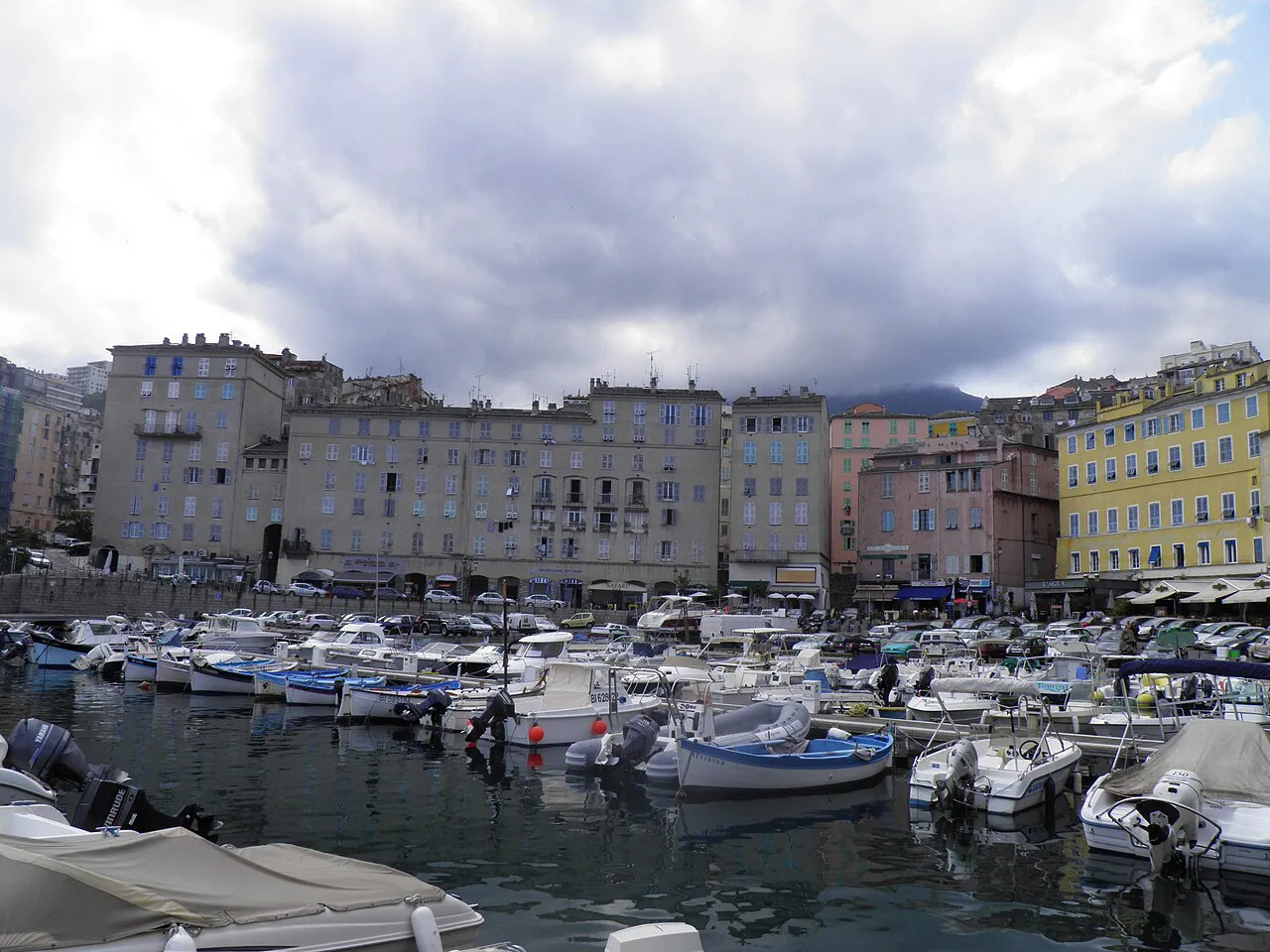 Row of tall pastel buildings behind small boats moored in the Old Port of Bastia