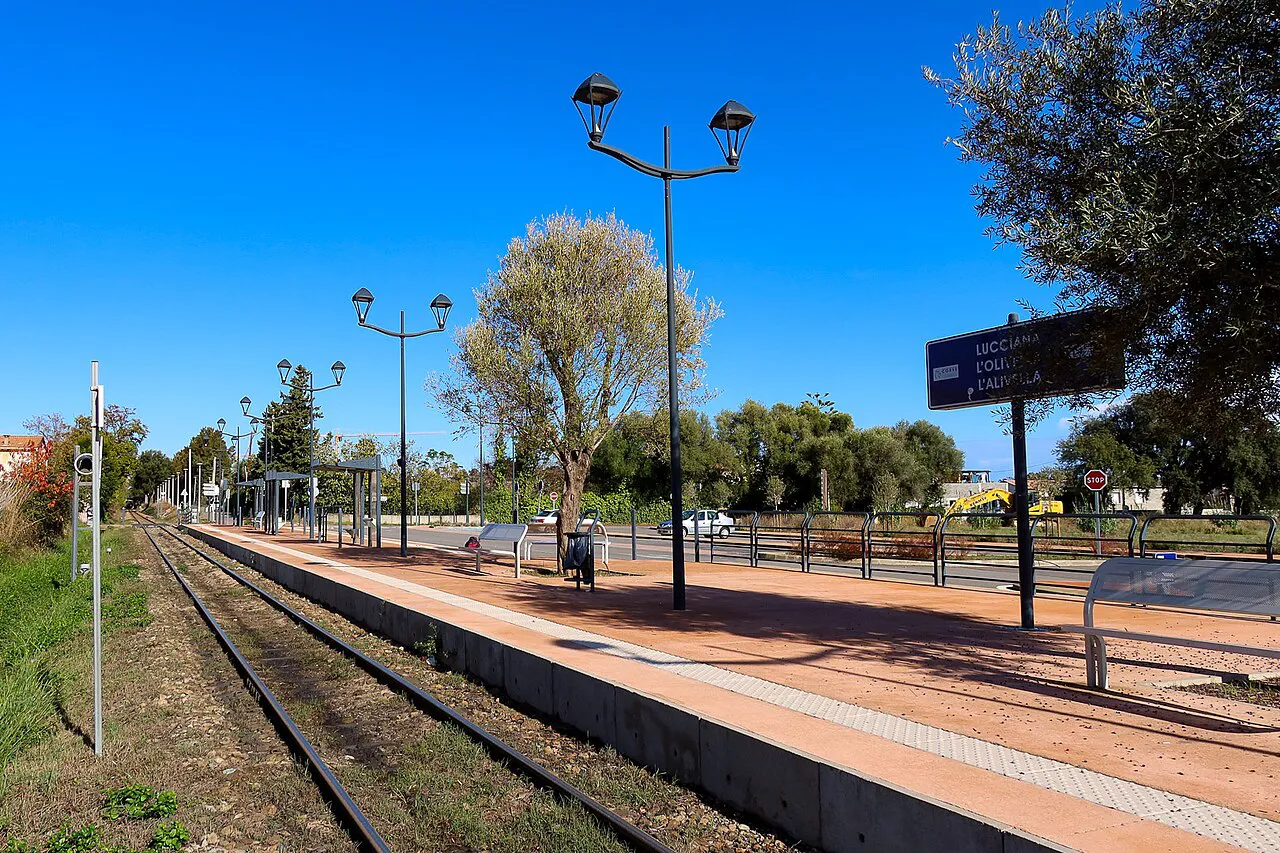 Single-track railway and platform at the L'Alivella train stop near Lucciana, Corsica, under a blue sky