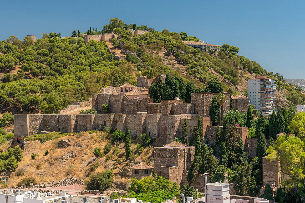 The Alcazaba of Málaga’s stone walls climbing a wooded hillside above the city
