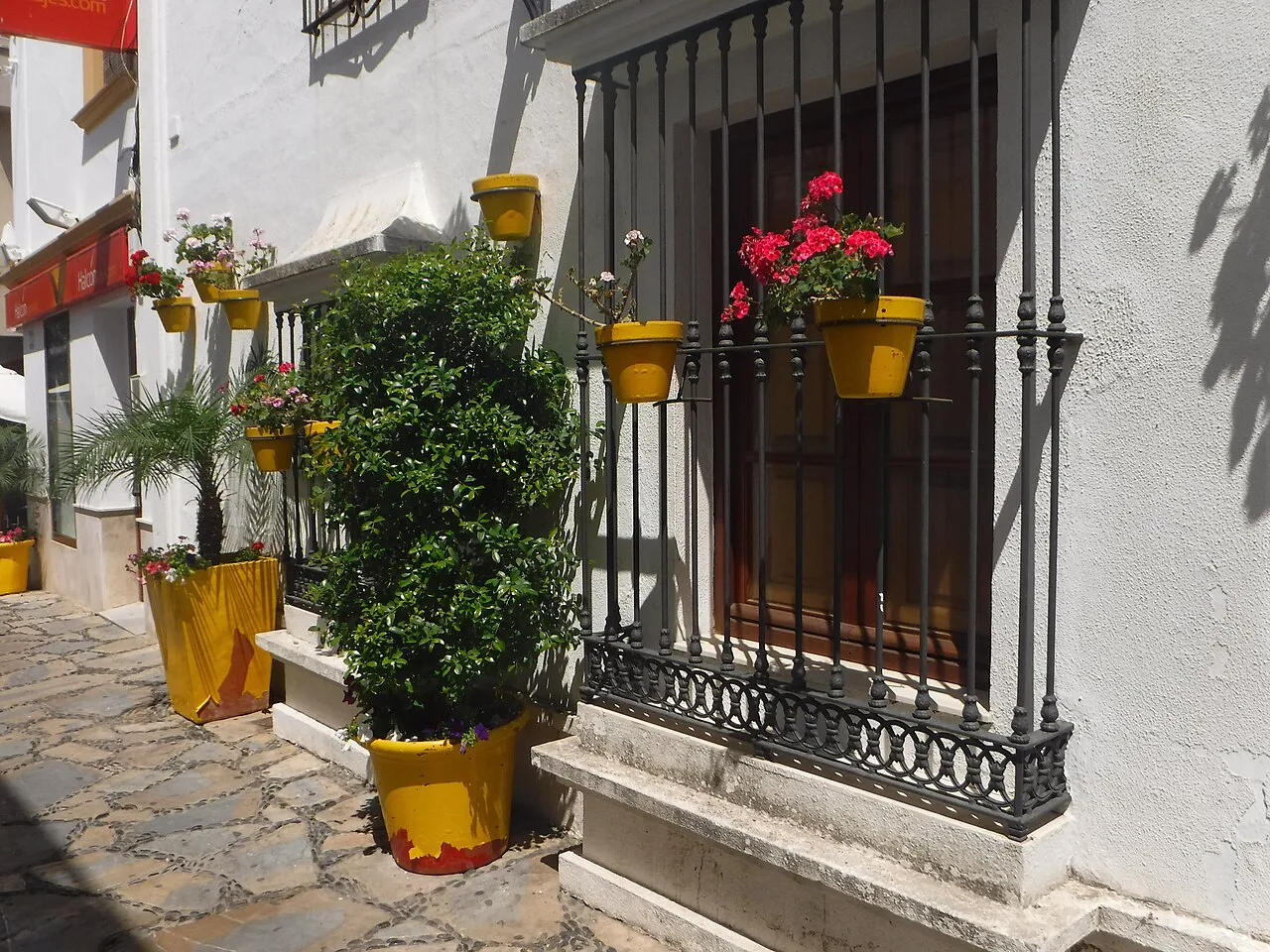 Whitewashed house with yellow flowerpots and red geraniums on a cobbled lane in Estepona old town