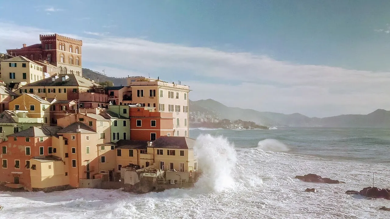 Colourful houses of Boccadasse on the rocks as waves break below, Genoa