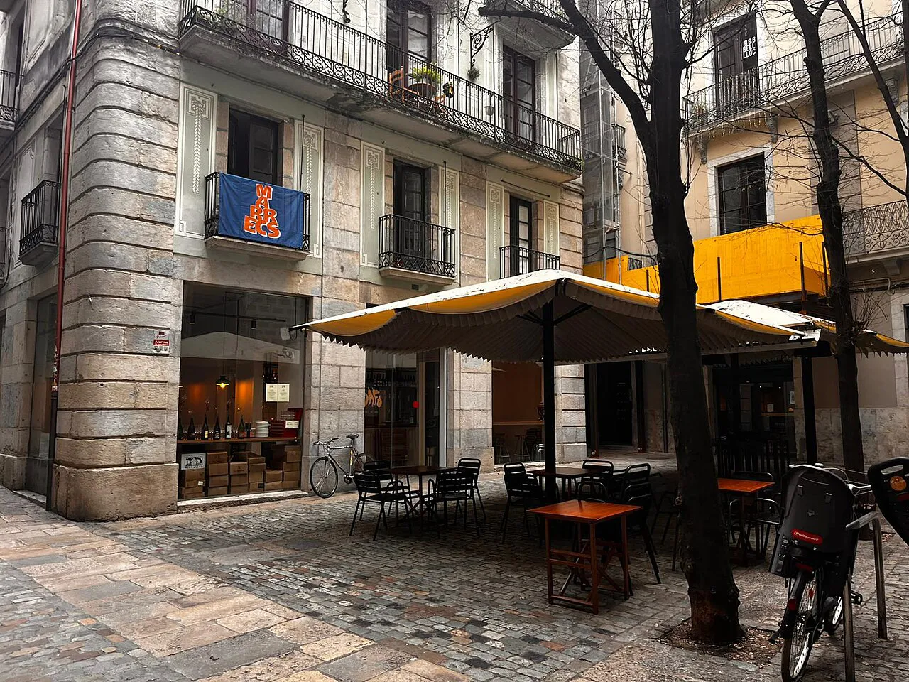Cobbled Plaça Bell-Lloc with café tables and old stone buildings in Girona’s Barri Vell