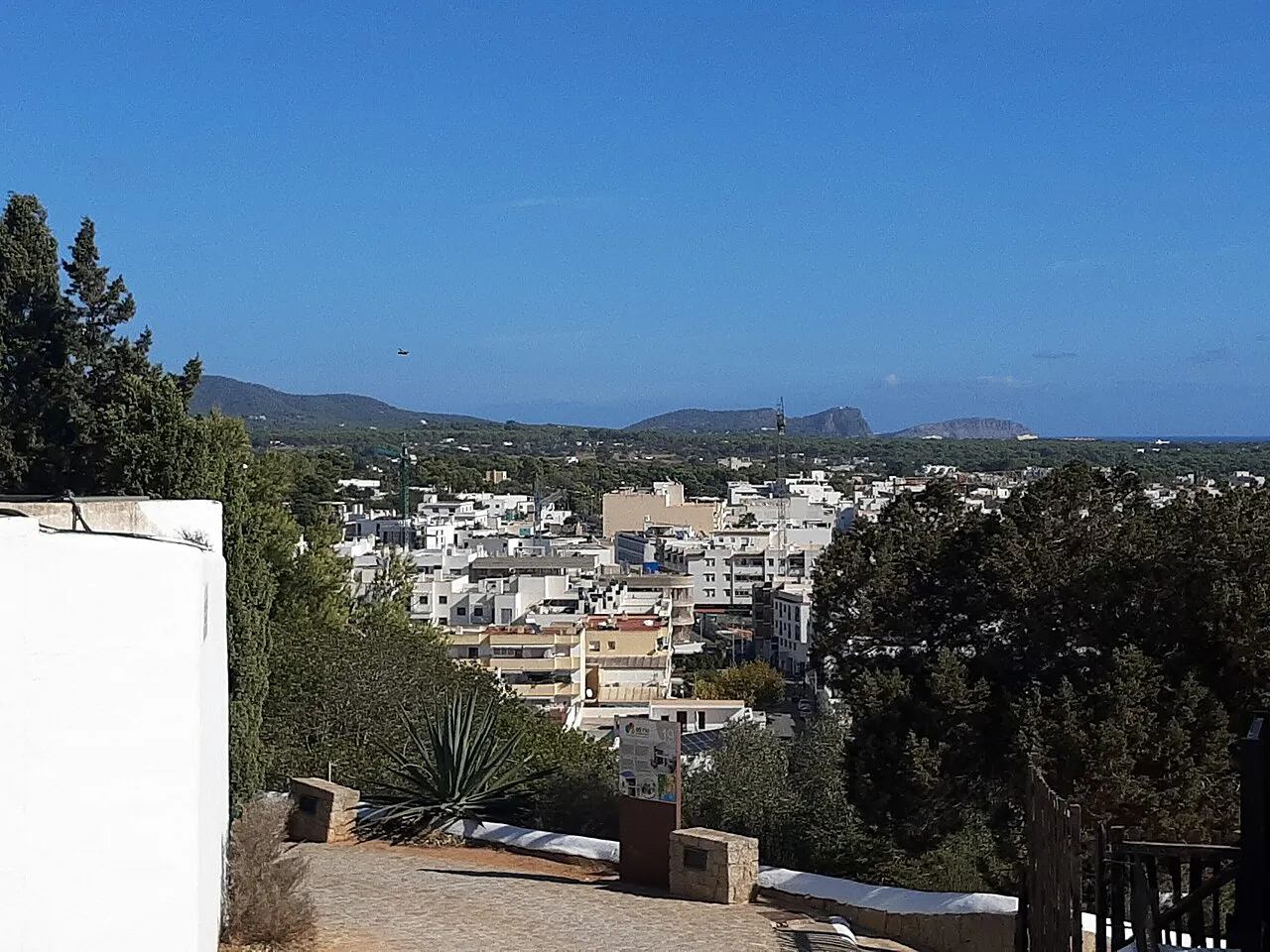 White town buildings of Santa Eulària des Riu seen from the church hill, with green hills and coast beyond