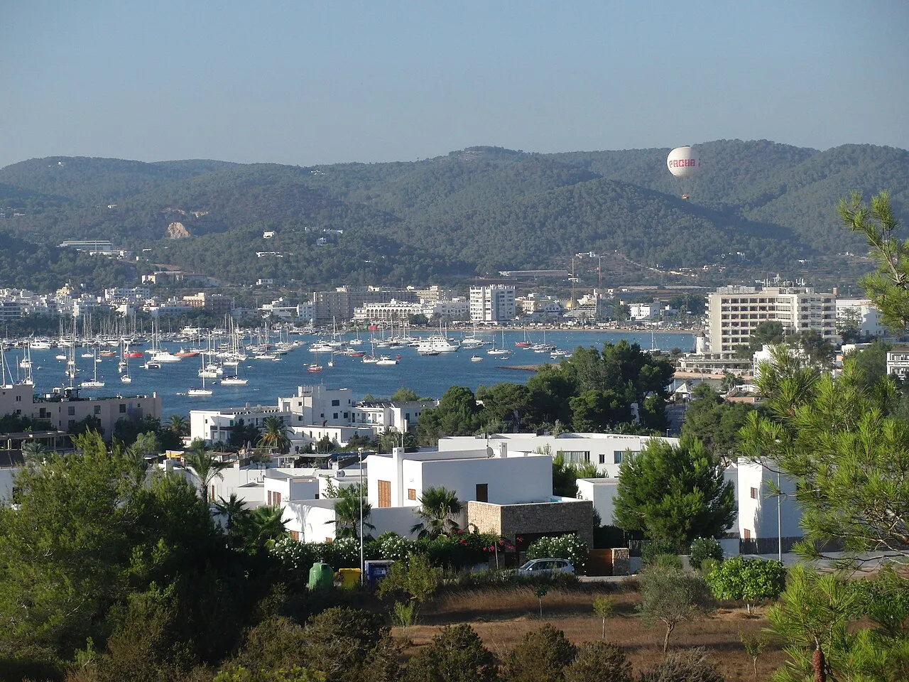 Sant Antoni bay with moored boats and white town buildings below wooded hills in Ibiza