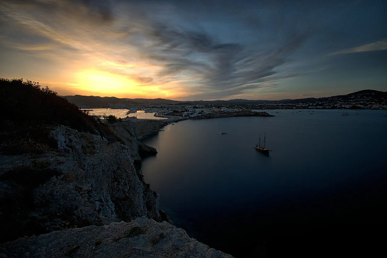 Sunset over Talamanca Bay from the rocky shore, with Ibiza Town lights across the water