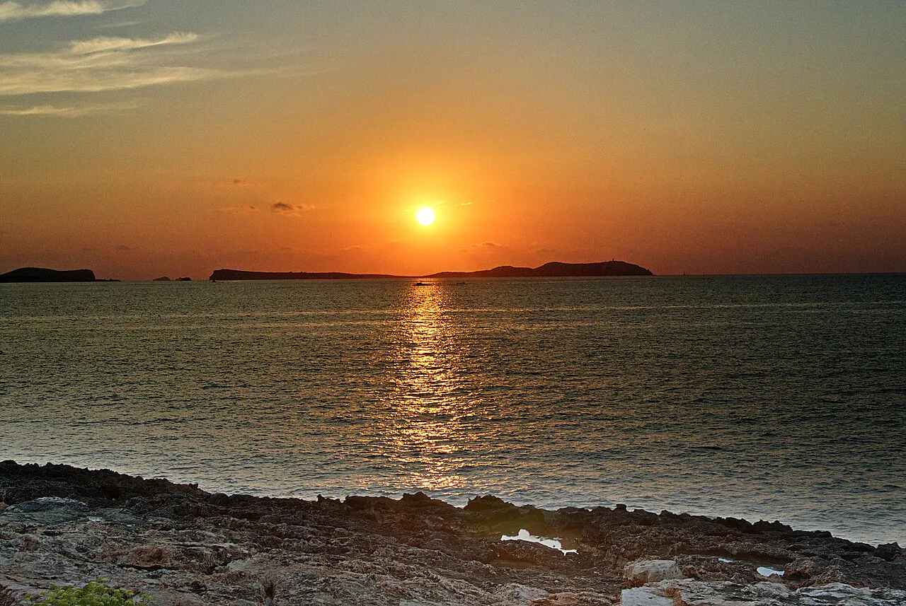 Sun setting over the sea and offshore islets, seen from the rocky shore at Sant Antoni, Ibiza