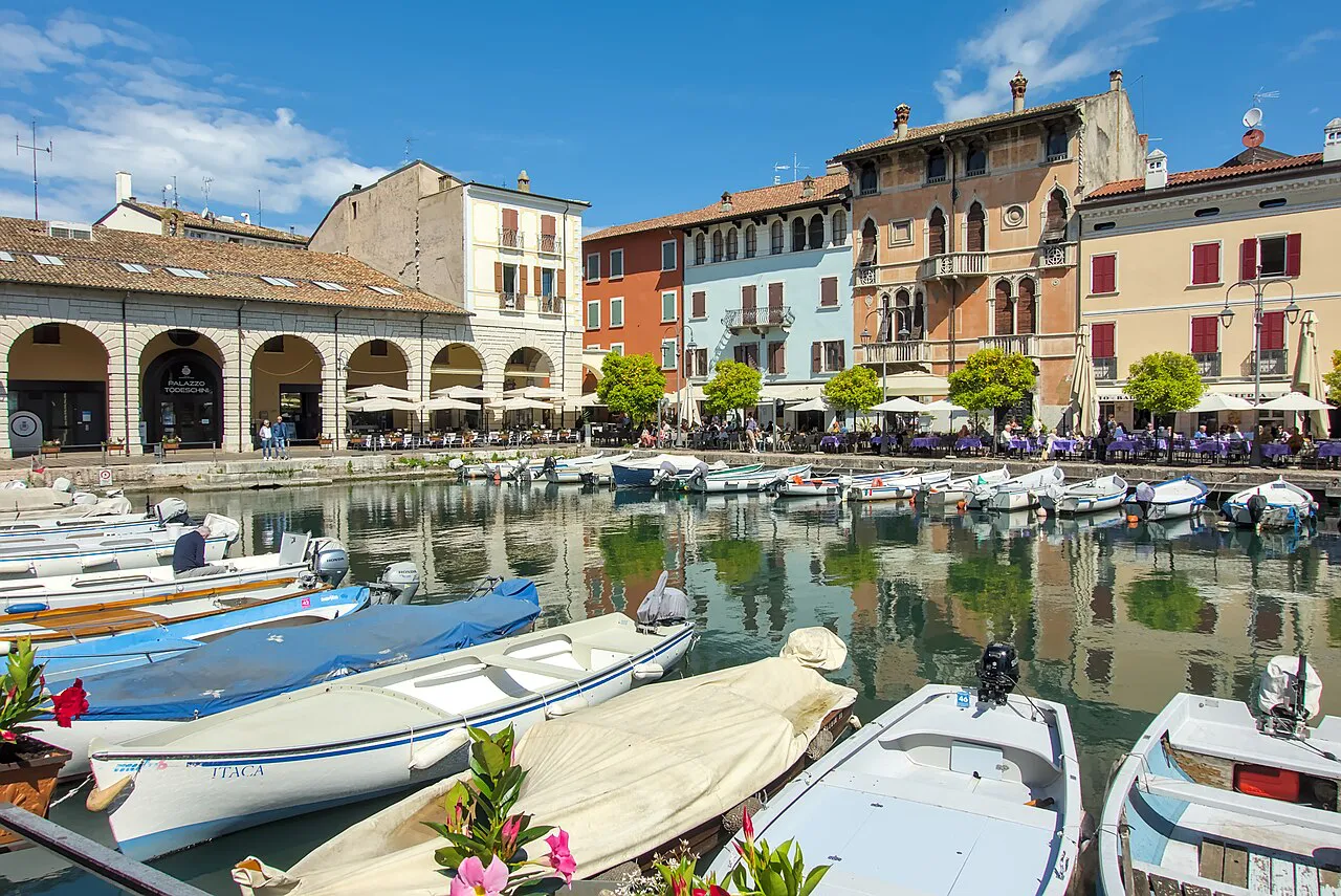 Small boats moored in the Porto Vecchio of Desenzano del Garda, lined with arcades and colourful houses