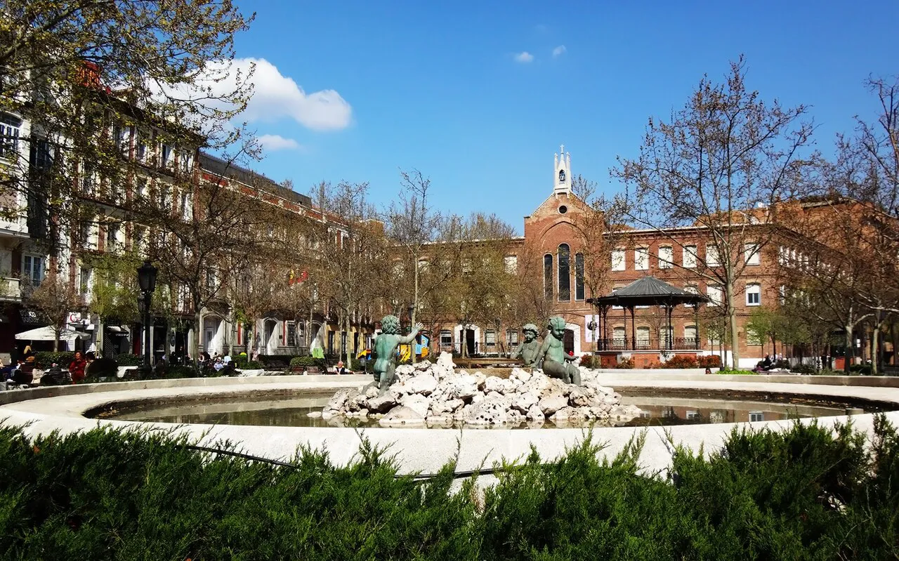 Fountain and red-brick buildings around Plaza de Chamberí in Madrid under a blue sky